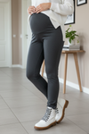 A pair of gray opriest sports maternity tights with a high waist, worn by a model standing sideways. The model is also wearing white boots with a lace-up front.