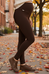 Person wearing brown leggings and shoes on a street with autumn leaves and trees.