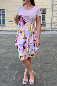 Woman in a colorful brestfeeding dress standing on a pavement with a building in the background